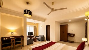 A hotel room with a bed, a desk, a chair, a TV, a wardrobe, and a ceiling fan. - Hotel Europa Inn (Rajkot)