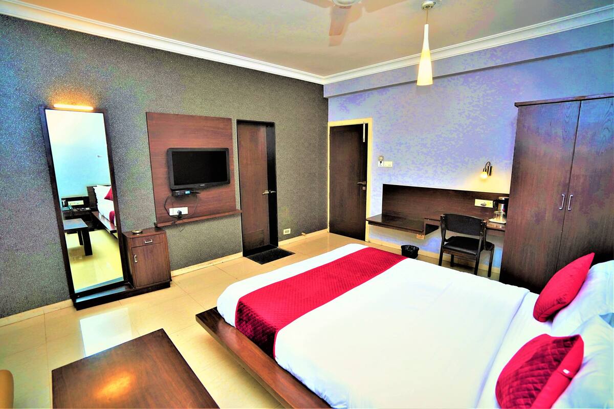A hotel room with a large bed, a desk, a chair, a TV, and a wardrobe.