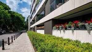 A modern building with a clean facade, a well-maintained sidewalk, and a row of potted plants with red flowers. - Apartamenty Sun & Snow Rezydencja Łazienki Park (Warsaw)