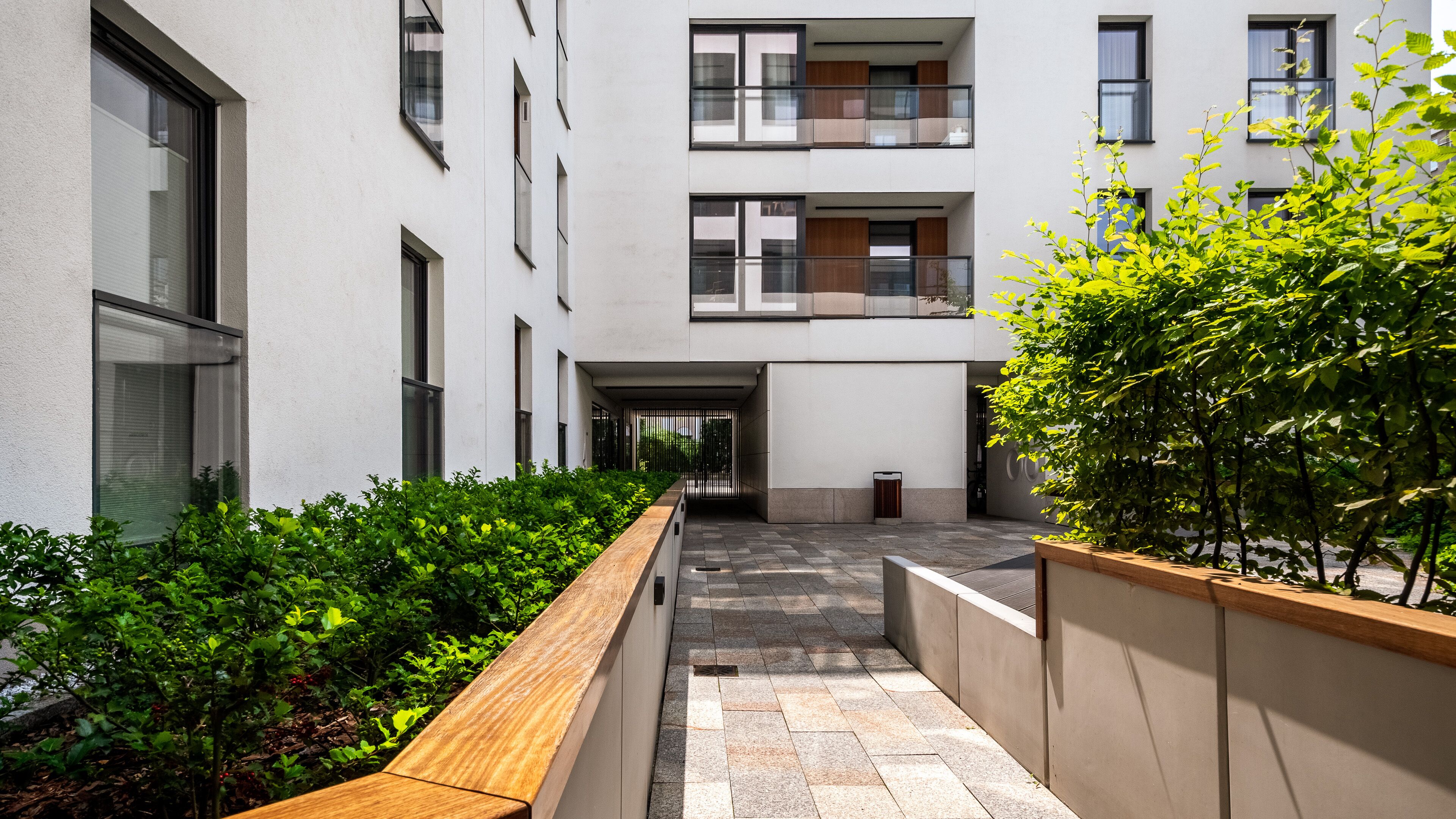 A modern building with multiple floors, large windows, and a central courtyard with a wooden bench and greenery.