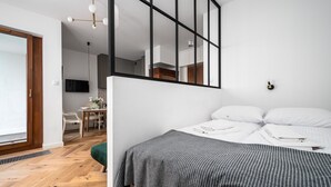 A modern bedroom with a bed, a dining area, and a kitchen visible through an open door. - Apartamenty Sun & Snow Rezydencja Łazienki Park (Warsaw)