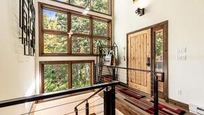 A spacious interior with large windows offering a view of a forest, a wooden staircase, and a modern light fixture.