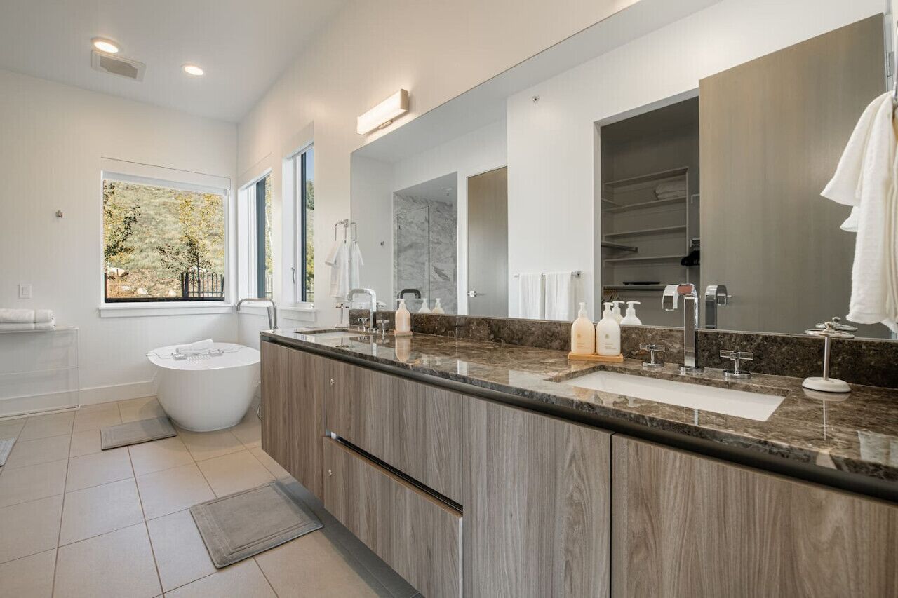 A modern bathroom with a freestanding bathtub, a large mirror, and a vanity with a marble countertop.