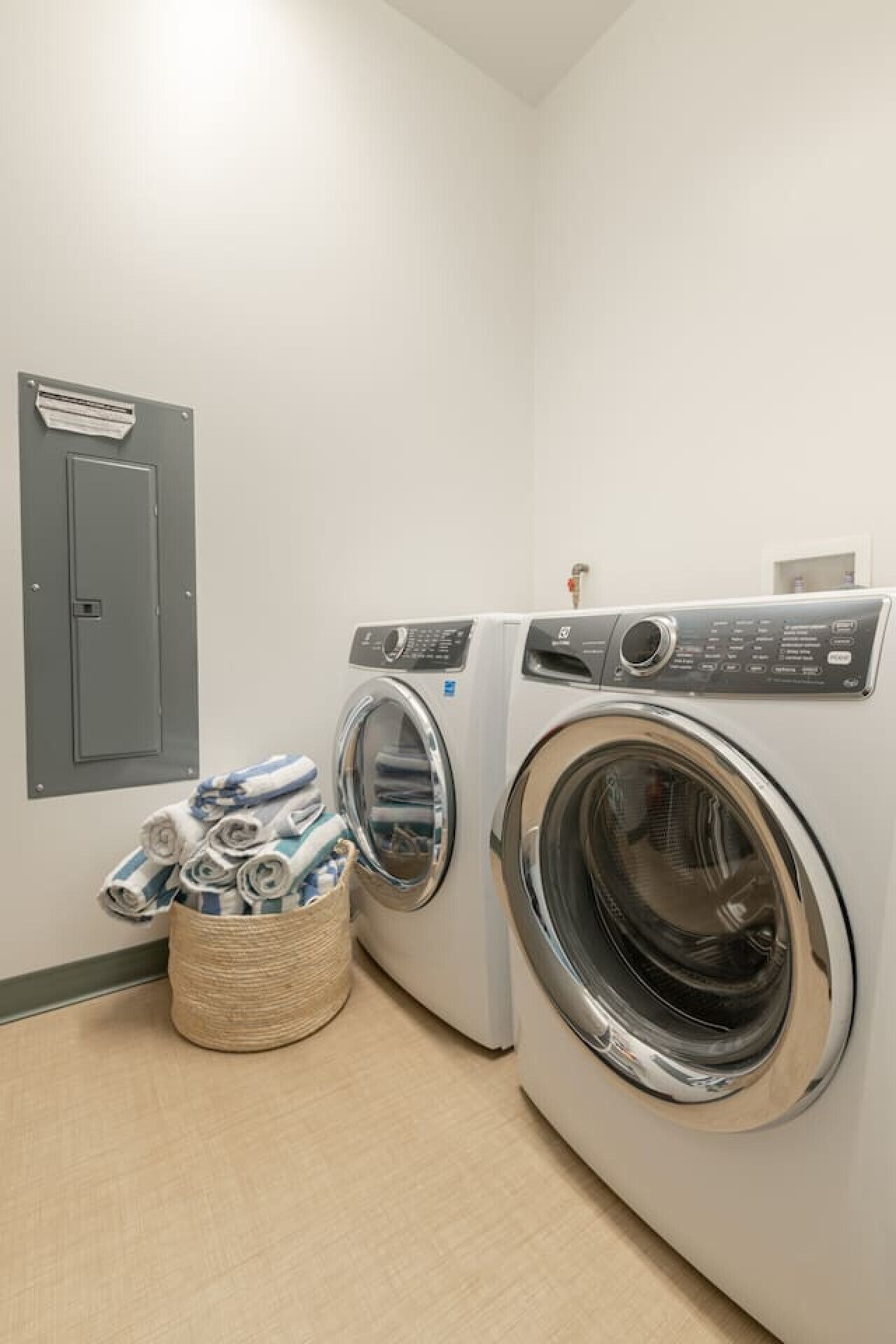 A laundry room with two front-loading washing machines, a small basket with folded towels, and a utility panel on the wall.