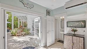 A spacious room with a large open door leading to a patio area, a white door, a mounted artwork, a wall-mounted TV, and a modern bathroom with a sink and mirror. - **SIREN'S SERENADE @ THE ANNEX** Home & Pool + Last Key White Glove Service... (Key West)