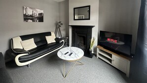 Ein modernes Wohnzimmer mit einem schwarzen Ledersofa, einem weißen Marmortisch, einem Kamin, einem angebrachten Fernseher, der Netflix zeigt, und einem Stadtbild an der Wand.