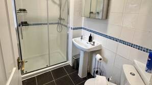 Ein Badezimmer mit einer Duschkabine, einem weißen Waschbecken, einer Toilette und einem Spiegel über dem Waschbecken.