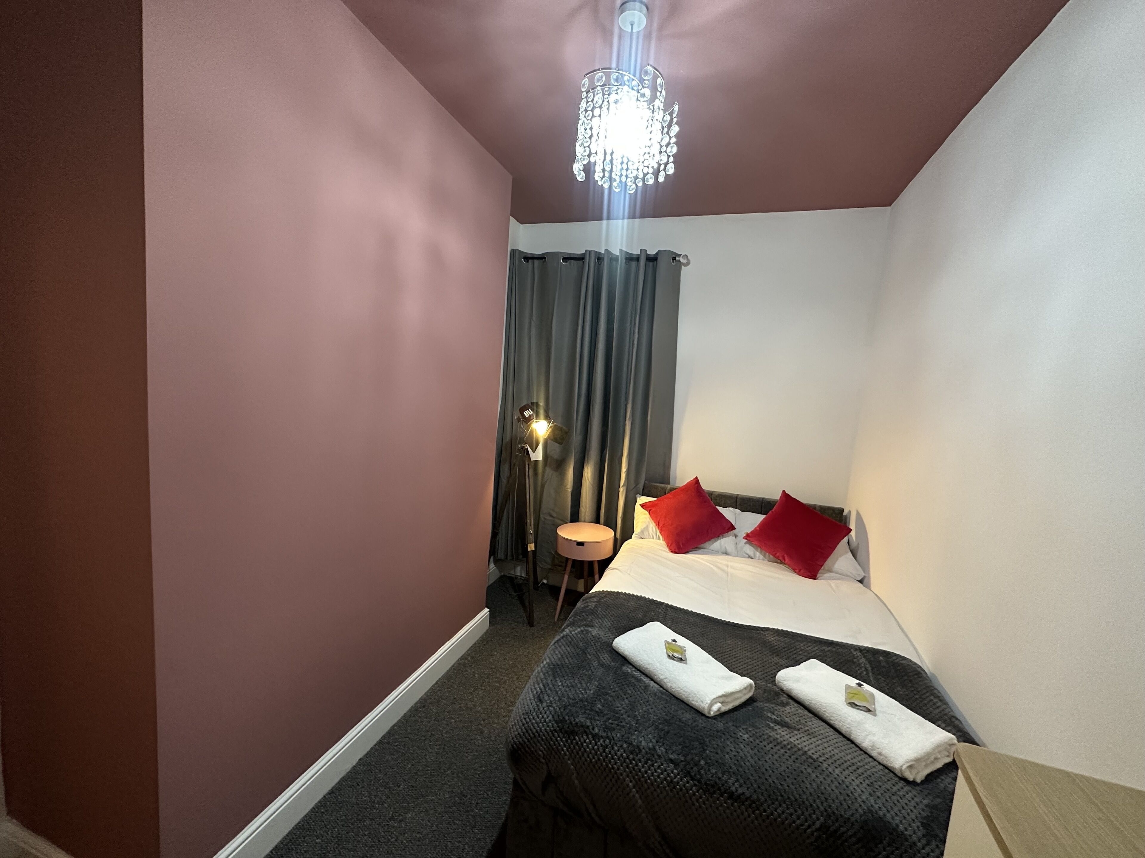 Quarto de hotel com cama, mesa de cabeceira, abajur e lustre.