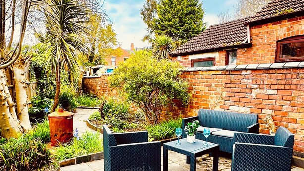 Eine Terrasse mit Gartenmöbeln, einer Ziegelwand und einem Garten mit verschiedenen Pflanzen.
