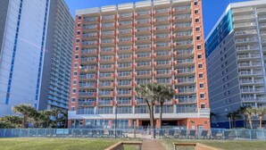 A multi-story hotel with a central atrium, balconies on each floor, and a surrounding fence. - RT-0703 Oceanfront 1-Bedroom Condo at Roxanne Towers, Myrtle Beach - Sleeps 6 (Myrtle Beach)