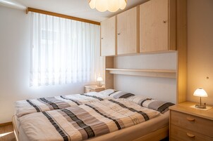 Un dormitorio con cama, mesitas de noche, armario y ventana con cortinas.