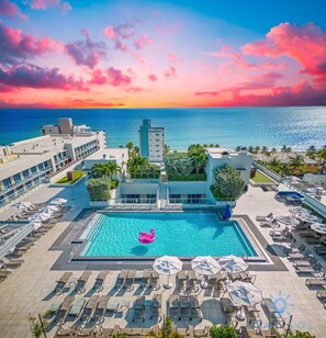 Un hôtel doté d’une piscine, de chaises longues et offrant une vue sur l’océan au coucher du soleil.