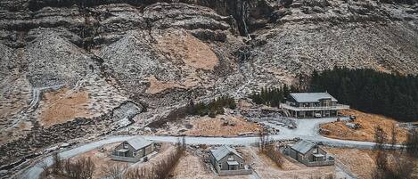 Un paysage isolé, recouvert de neige, avec une grande maison entourée de bâtiments plus petits, probablement une propriété de vacances ou un lieu de retraite.