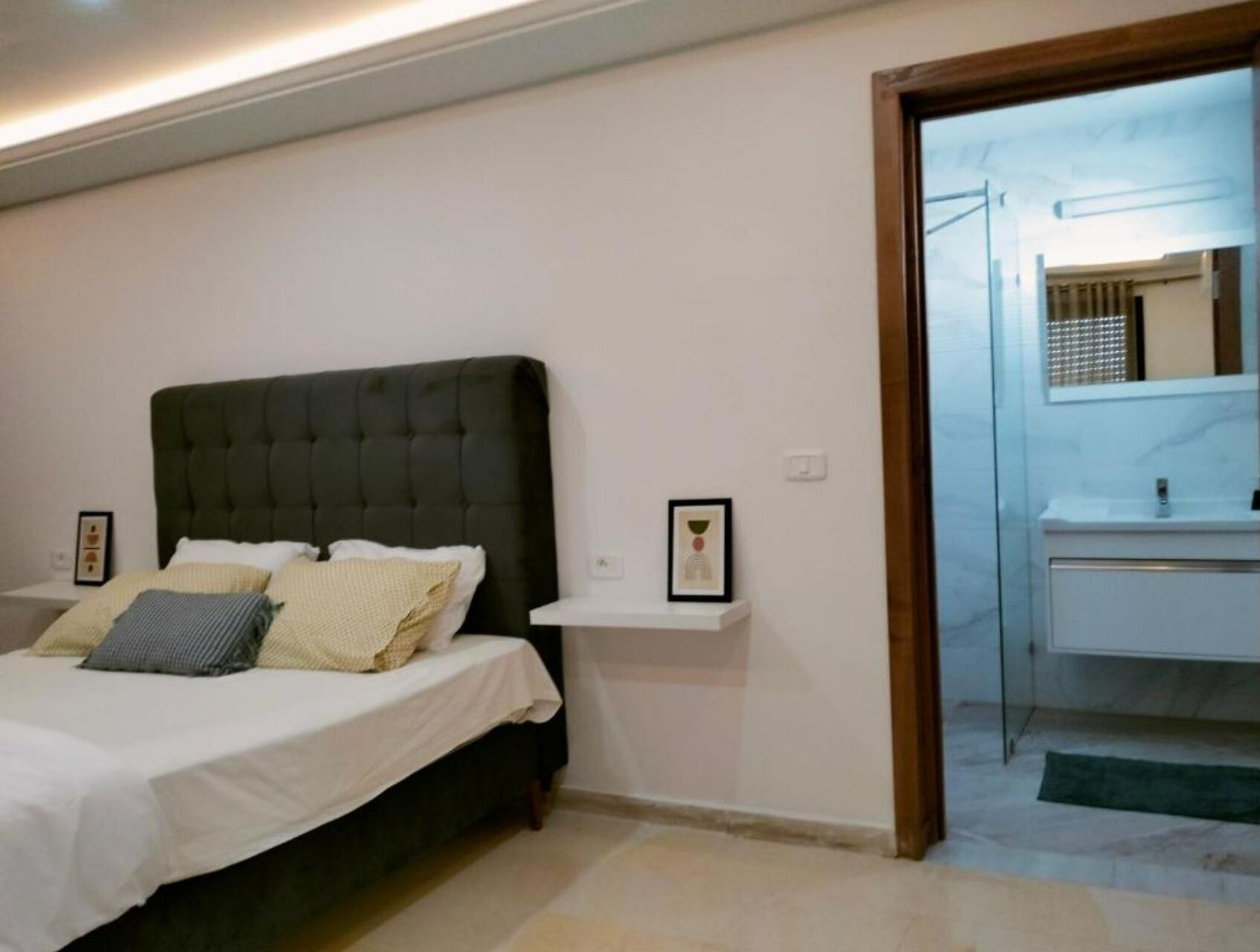 Een slaapkamer met een bed, een nachtkastje, een ingelijste foto en een zichtbare badkamer door een geopende deur.