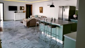 A modern kitchen with a central island, bar stools, and a dining area with a sofa. - Villa Agate (Médenine)