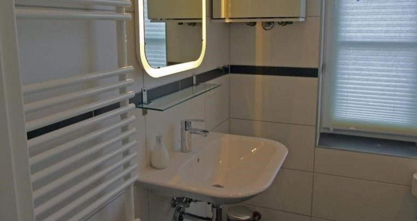 A bathroom with a white sink, a mirror with a lighted frame, and a towel rack.