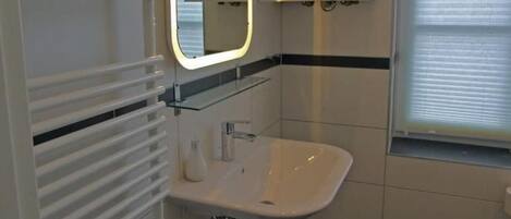 A bathroom with a white sink, a mirror with a lighted frame, and a towel rack.