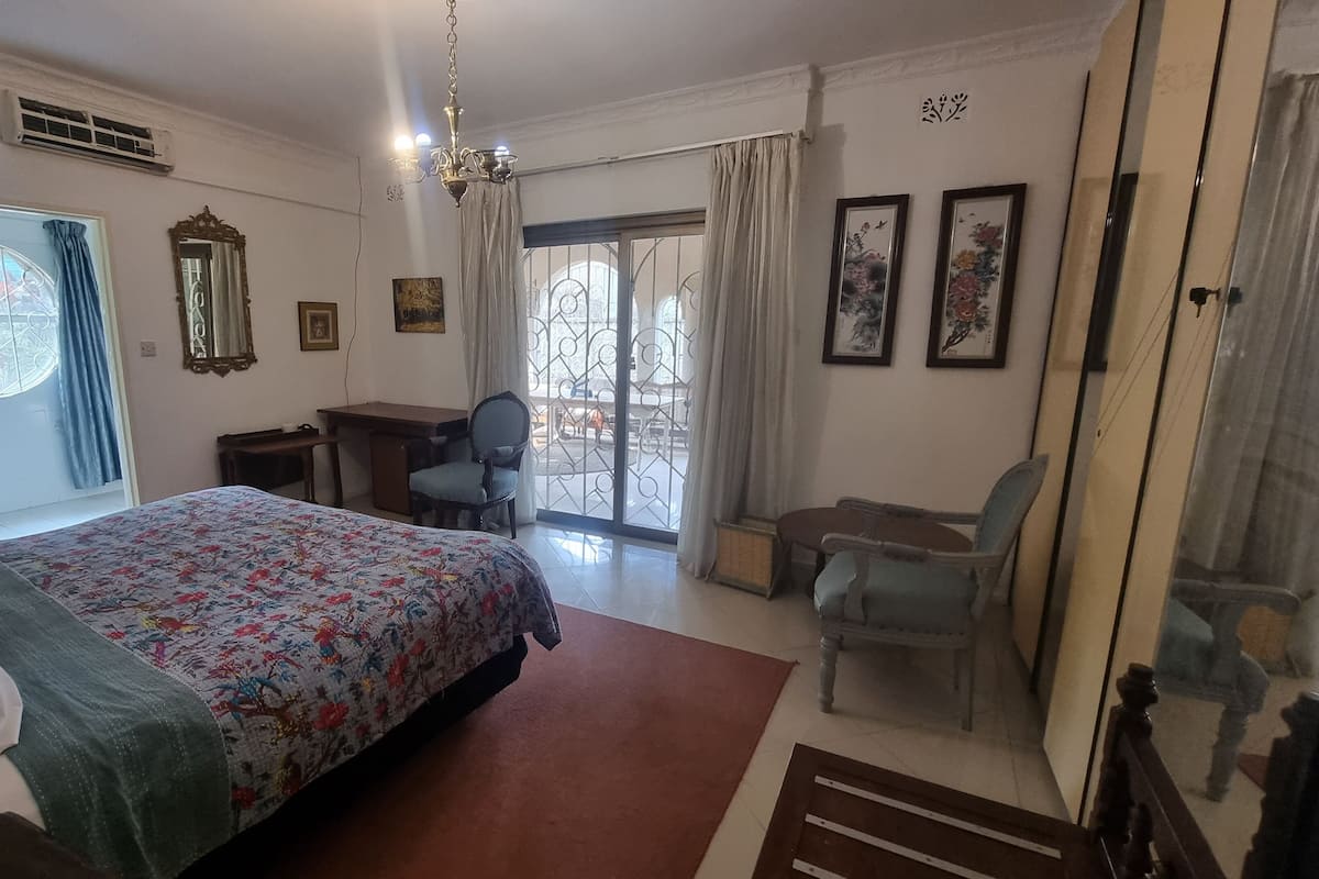 A bedroom with a bed, a desk, a chair, and a balcony with a view.