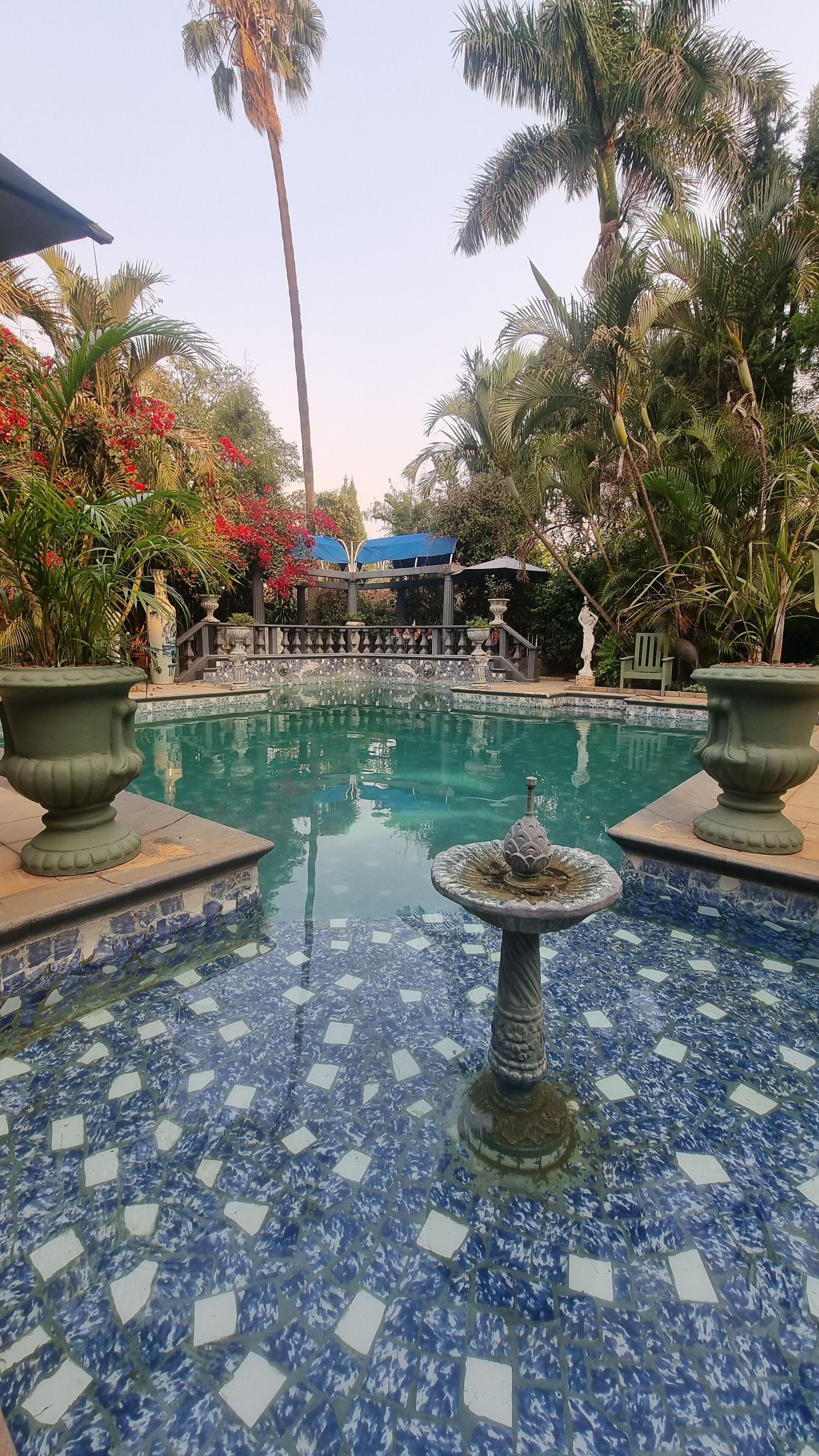 A pool area with a fountain, surrounded by palm trees and a tiled floor.