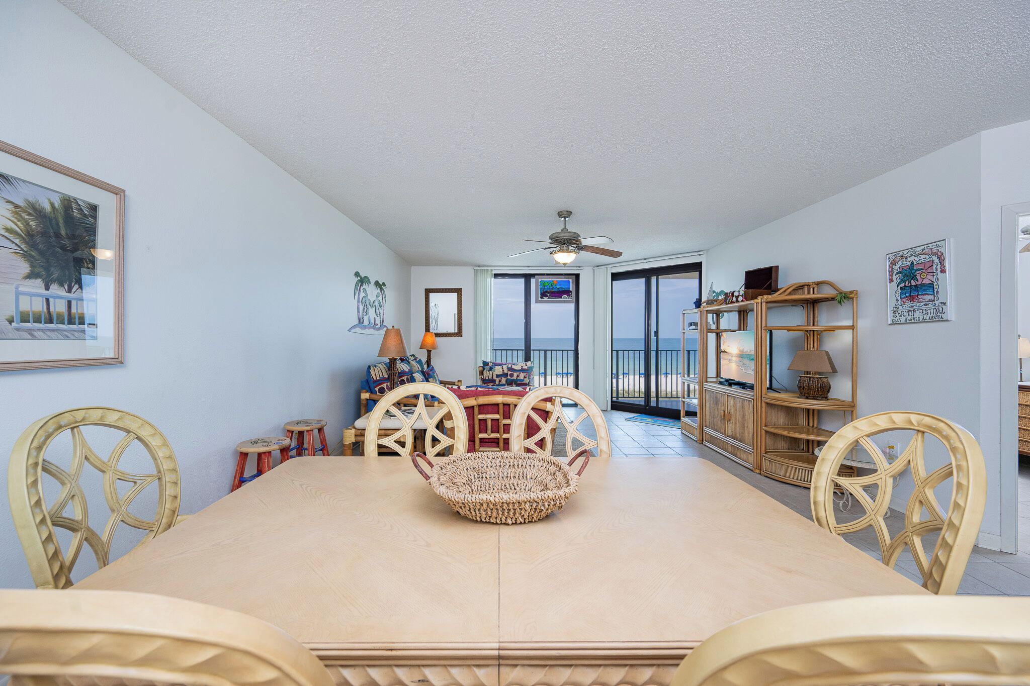 Un espace repas avec une grande table, des chaises en osier et un ventilateur de plafond.