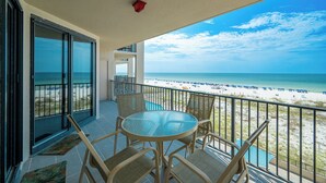 A balcony with a glass table and chairs overlooking a beach.