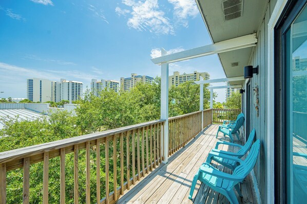 A wooden deck with blue chairs, a white railing, and a view of high-rise buildings in the background.
