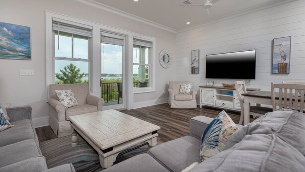 A spacious living room with a large TV, comfortable seating, and a view of the outdoors. - West Side Cottages N - Your Gulf Shores Paradise Awaits (Gulf Shores)