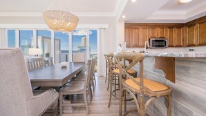 A modern kitchen with wooden cabinets, a large island, and a dining area with a view. - Condo at Phoenix Orange Beach II, Brand New! (Orange Beach)