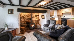 A cozy living room with a stone fireplace, leather sofas, and a kitchen in the background.