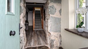 A stone-walled hallway leading to a staircase, a door, and a window with a potted plant.