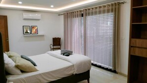 A bedroom with a bed, a chair, a wardrobe, and a window with blinds. - Villa Agate (Djerba)