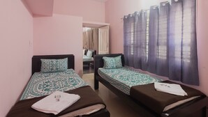 A room with two beds, each with patterned bedding, a ceiling fan, and a window with curtains. - JnJ Homestay (Chikkamagaluru)