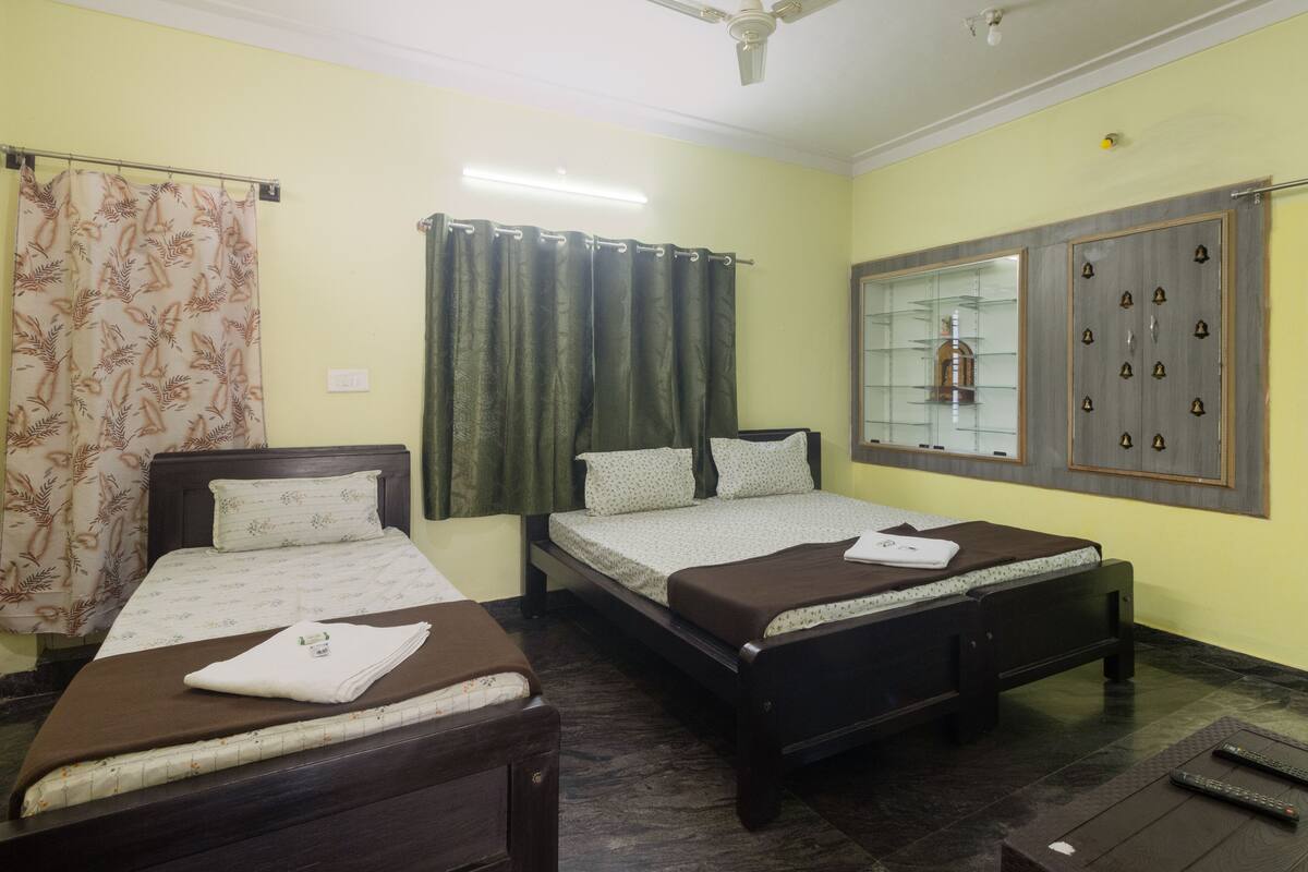A hotel room with two single beds, a ceiling fan, a window with a decorative metal frame, and a small shelf with items.