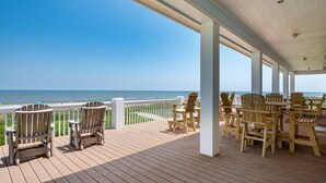 A covered outdoor deck with wooden chairs and tables, overlooking the ocean.