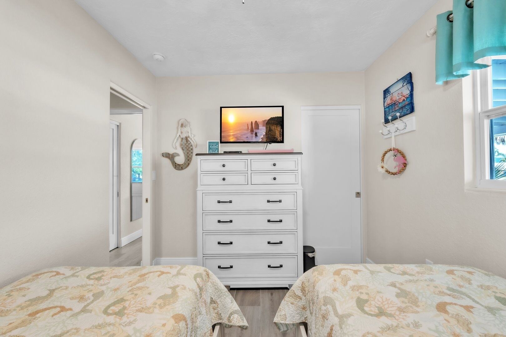 A bedroom with two beds, a dresser, a TV, and a window with curtains.