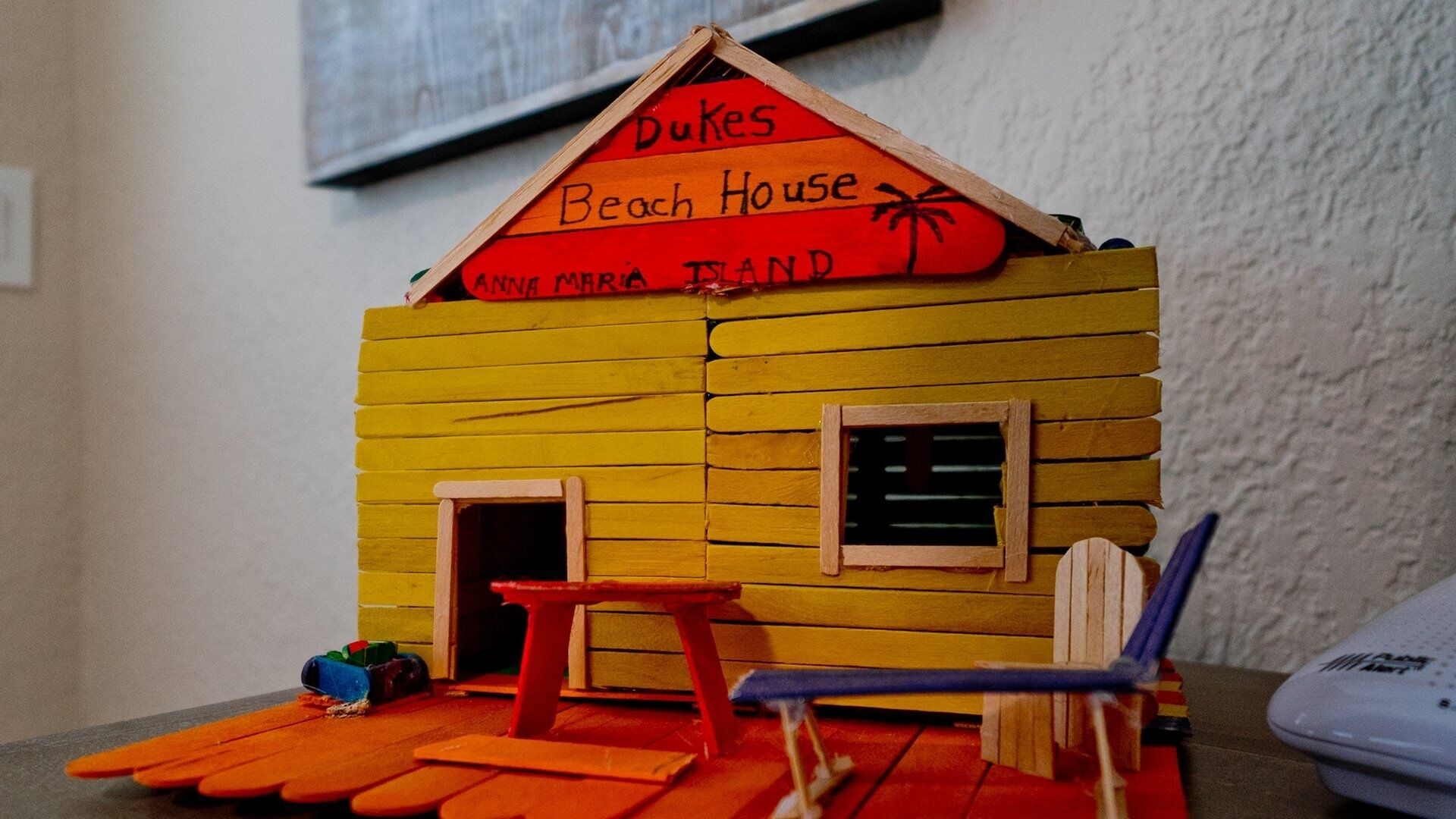 A small wooden model of a beach house with a sign reading "Dukes Beach House" and "Anna Maria Island."