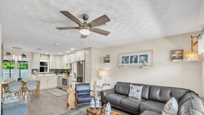 A modern living room with a grey sofa, a wooden coffee table, and a ceiling fan. - Seaduction Ami A 2 Bedroom Condo by RedAwning (Holmes Beach)