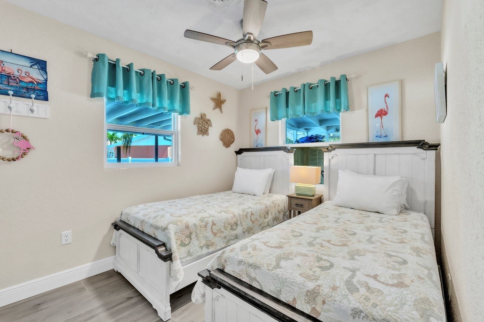 A bedroom with two beds, a ceiling fan, teal curtains, and a window with a view.