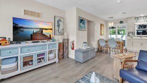 A living room with a TV, wooden cabinet, and a dining area with chairs and a table. - Seaduction Ami A 2 Bedroom Condo by RedAwning (Holmes Beach)