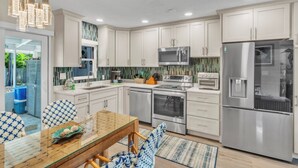A modern kitchen with white cabinets, stainless steel appliances, and a glass dining table. - Seaduction Ami A 2 Bedroom Condo by RedAwning (Holmes Beach)