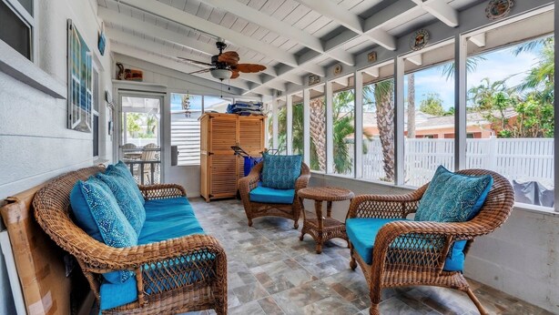 A covered patio with wicker furniture, a ceiling fan, and large windows offering a view of the surrounding area. - Seaduction Ami A 2 Bedroom Condo by RedAwning (Holmes Beach)