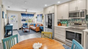 A modern kitchen with stainless steel appliances, a dining area with a wooden table, and a living room with a sofa and chairs. - Seaduction Ami B 2 Bedroom Condo by RedAwning (Holmes Beach)