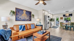 A living room with a brown leather sofa, a wooden coffee table, and a ceiling fan. - Seaduction Ami B 2 Bedroom Condo by RedAwning (Holmes Beach)