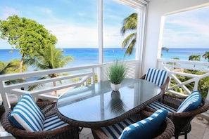 A balcony with wicker furniture, a glass table, and a view of the ocean.