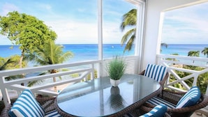 Een balkon met rieten meubels, een glazen tafel en uitzicht op de oceaan.