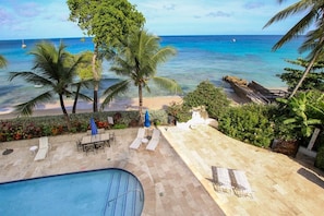 A pool area with lounge chairs and a view of the ocean.
