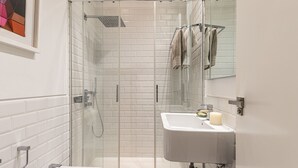 Casa de banho moderna com chuveiro de vidro, lavatório branco e espelho.