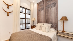 Quarto com uma cama grande, cabeceira de madeira, janela com cortinas e mesa de cabeceira com abajur.