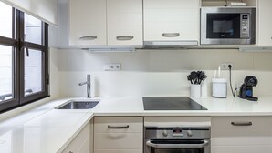 Uma cozinha moderna com armários brancos, micro-ondas de aço inoxidável, forno e pia.