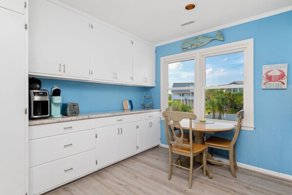Une cuisine avec des meubles blancs, un mur bleu et une fenêtre donnant sur un quartier résidentiel.